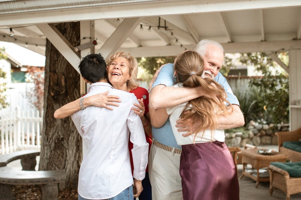 an-elderly-couple-embracing-their-son-and-daughter-6148876 A joyful family reunion outdoors with warm hugs and smiles under a wooden pergola.