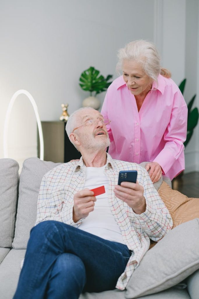 an-elderly-couple-having-conversation-at-the-living-room-7545225 Elderly couple using a mobile phone and credit card for online shopping at home.