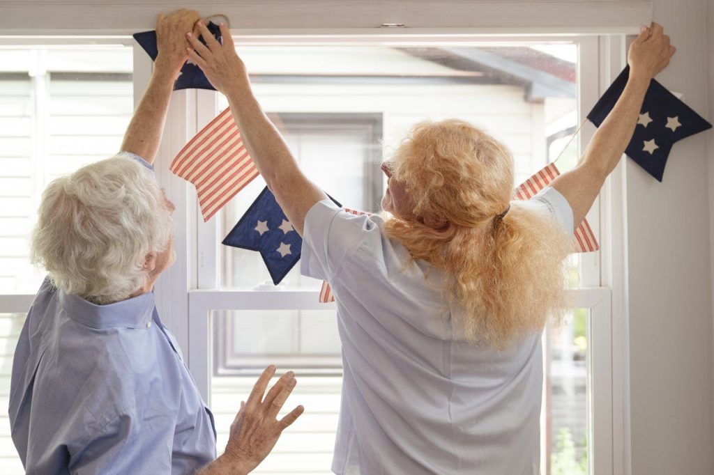 elderly-couple-hanging-american-flag-by-the-window-8805998 Senior couple hangs patriotic bunting in home for Independence Day celebration.